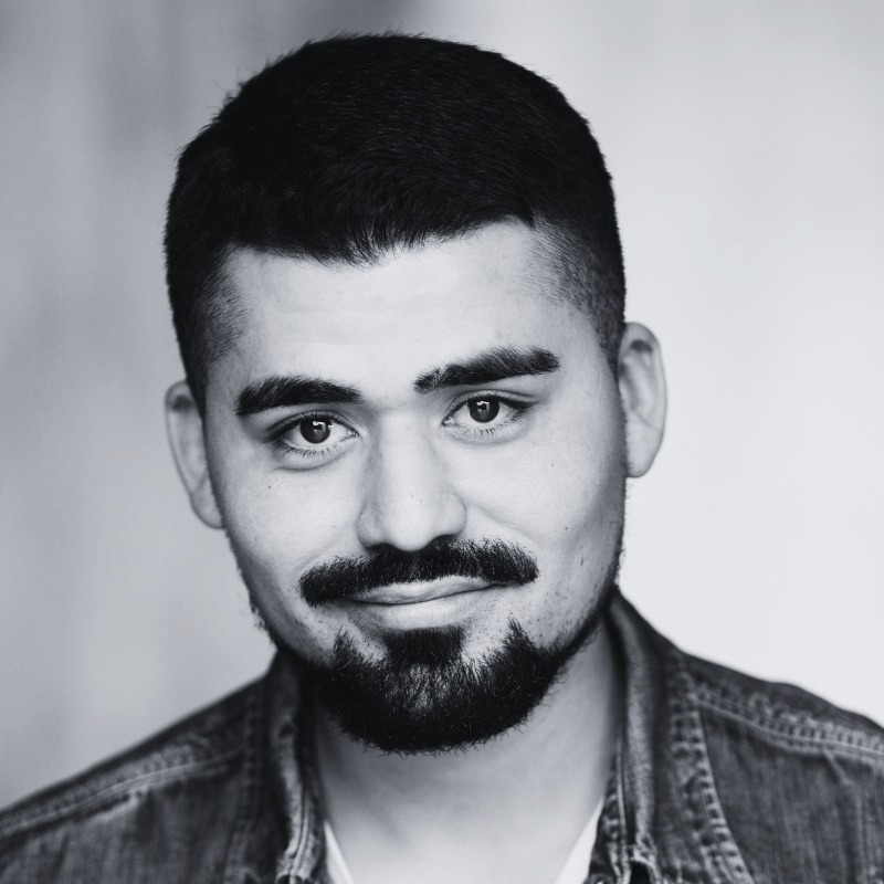 Monochrome portrait of a man with a beard and short hair, looking directly at the camera with a neutral expression.